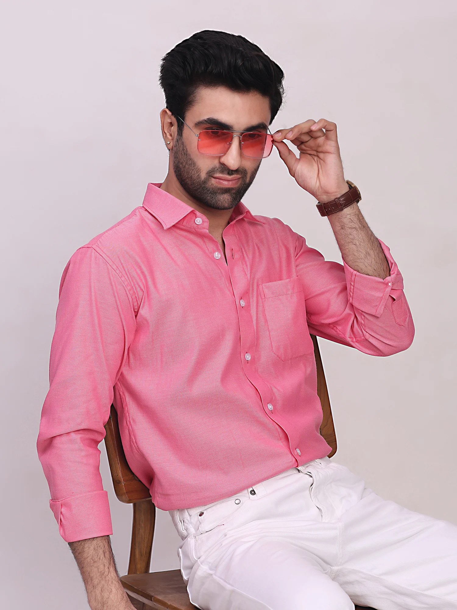 Model sitting in a chair wears a pink long-sleeve shirt with collar and chest pocket