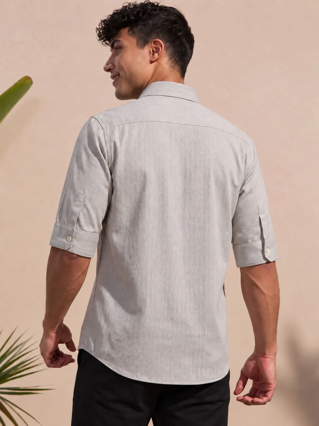 Back view of a male model wearing a taupe shirt with chevron pattern and rolled-up sleeves