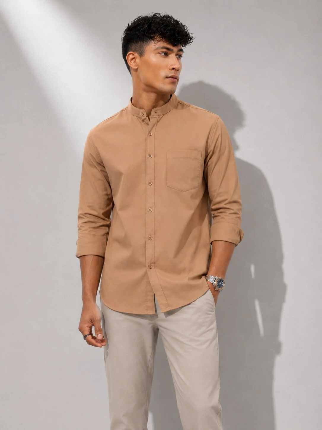 Tan coloured kurta with mandarin collar, long sleeves, chest pocket, and buttons down front, worn by a model