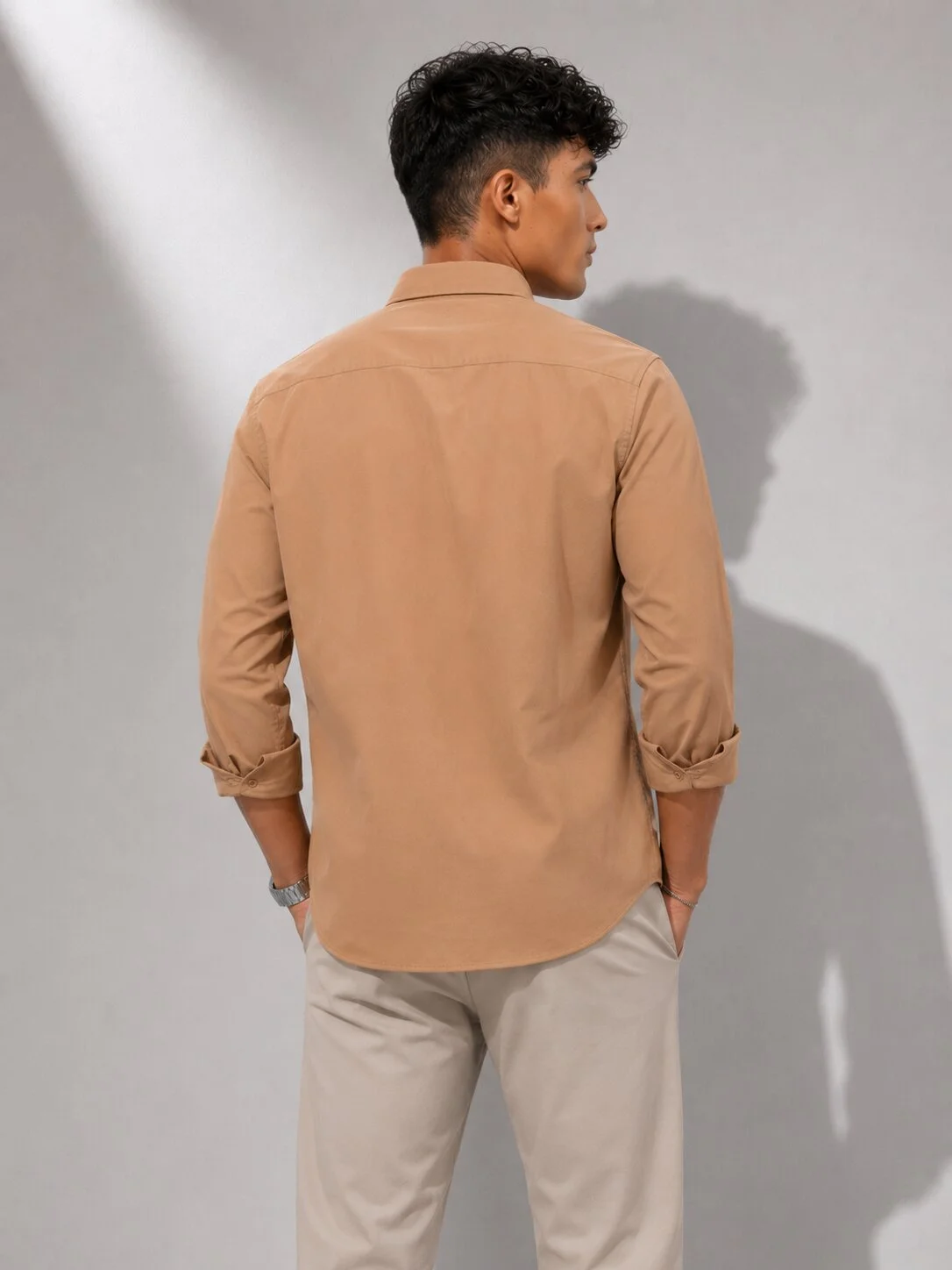 Back view of a male model wearing a peach long-sleeved shirt and trousers