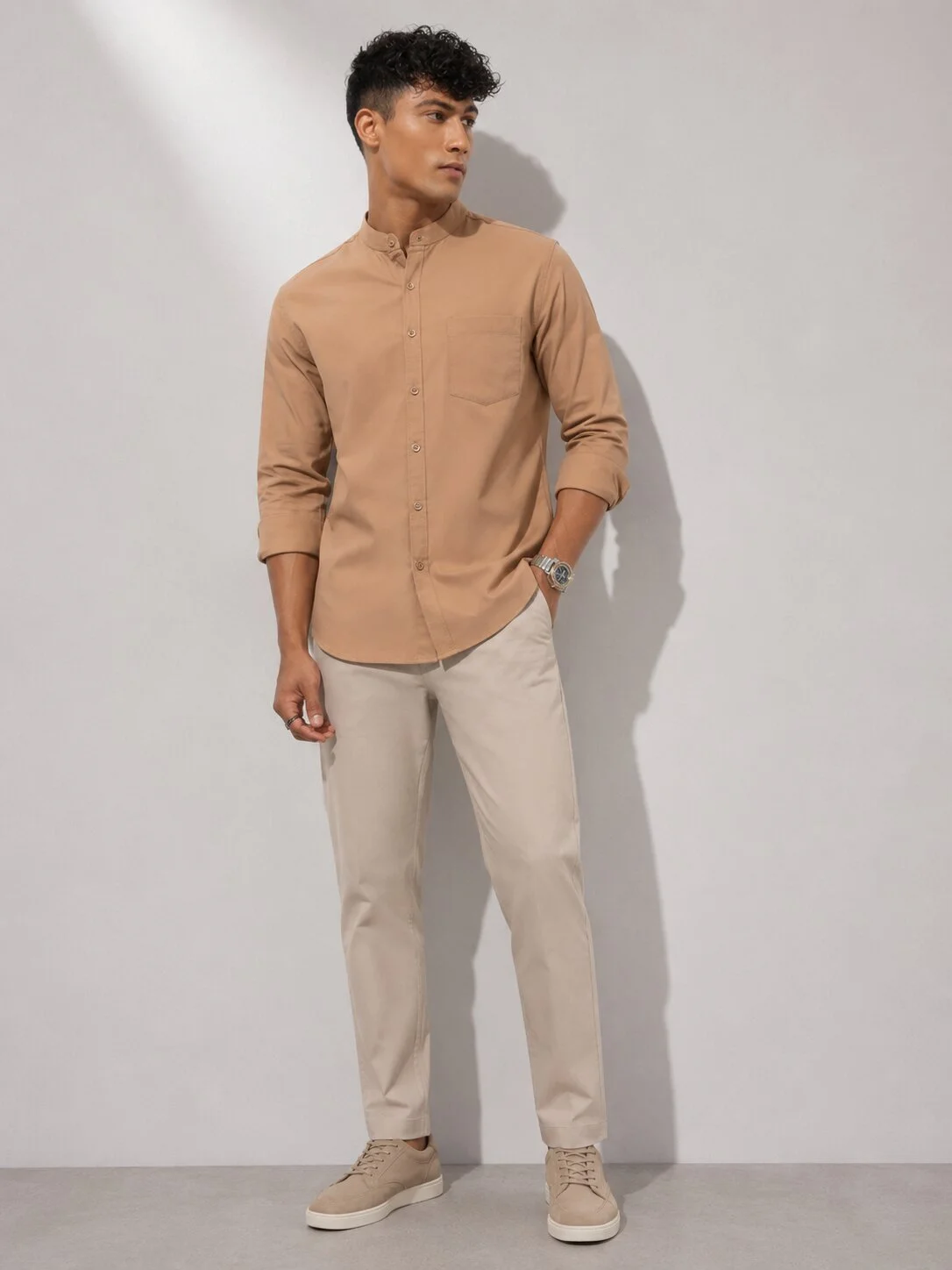 Model wearing a peach short kurta with mandarin collar, chest pocket, and full sleeves, paired with light trousers