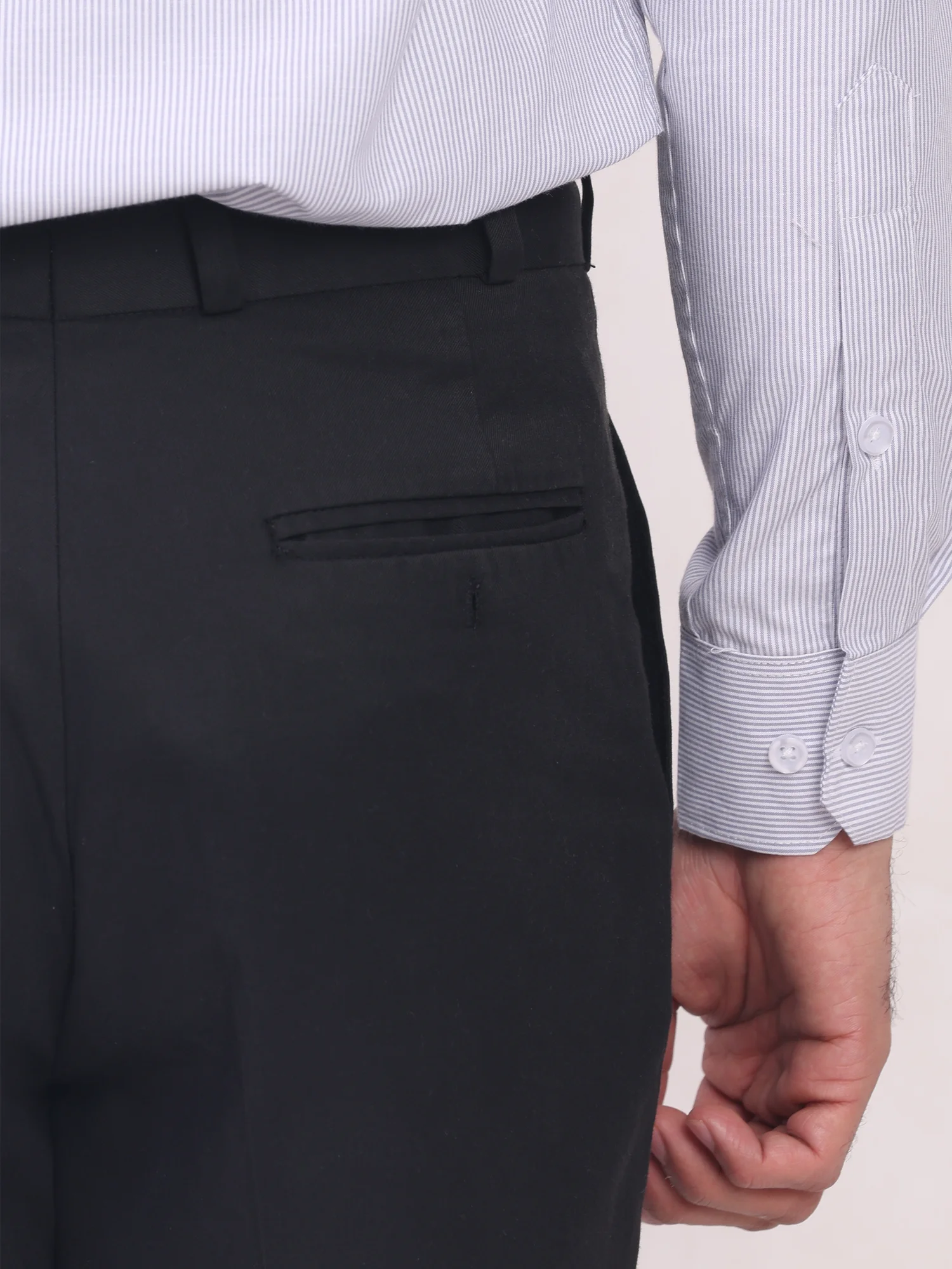 Black trousers, side view, back pocket, belt, buttons on cuff of light blue and white striped shirt