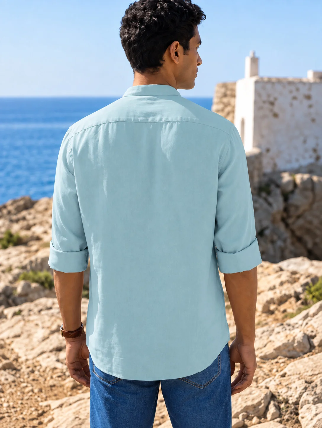 Back view of a model wearing a sea green long-sleeve shirt with rolled-up cuffs, collar, and blue jeans outdoors