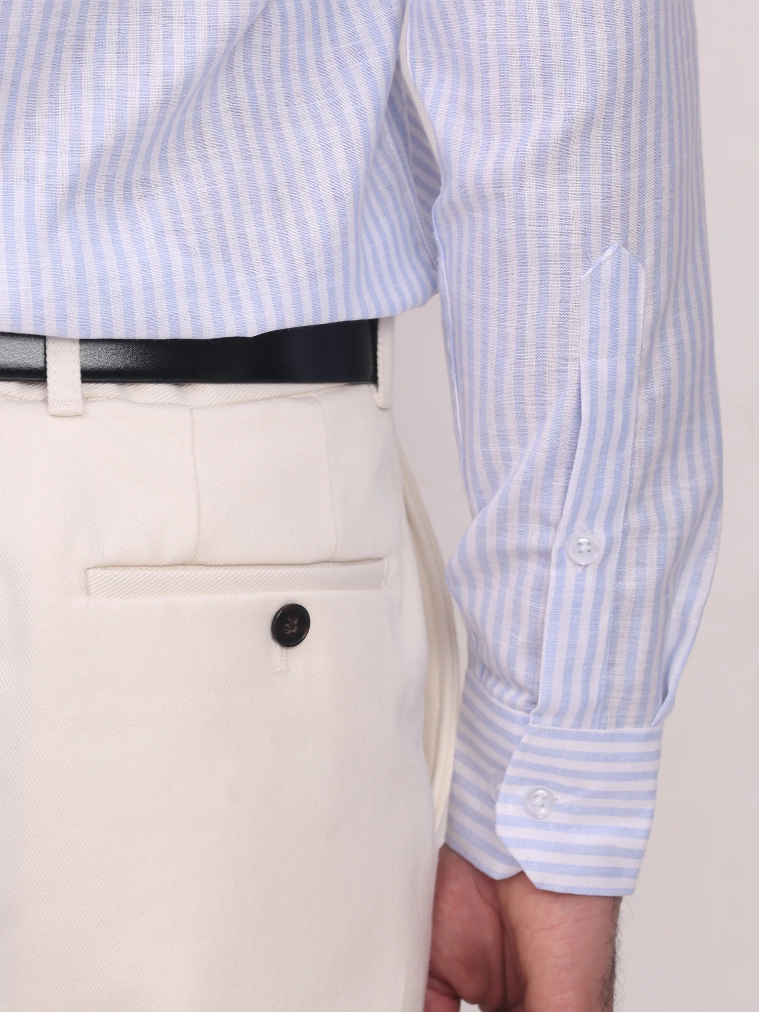 Light blue and white striped long-sleeve shirt, cuffed sleeves, buttons, worn by a model with beige pants