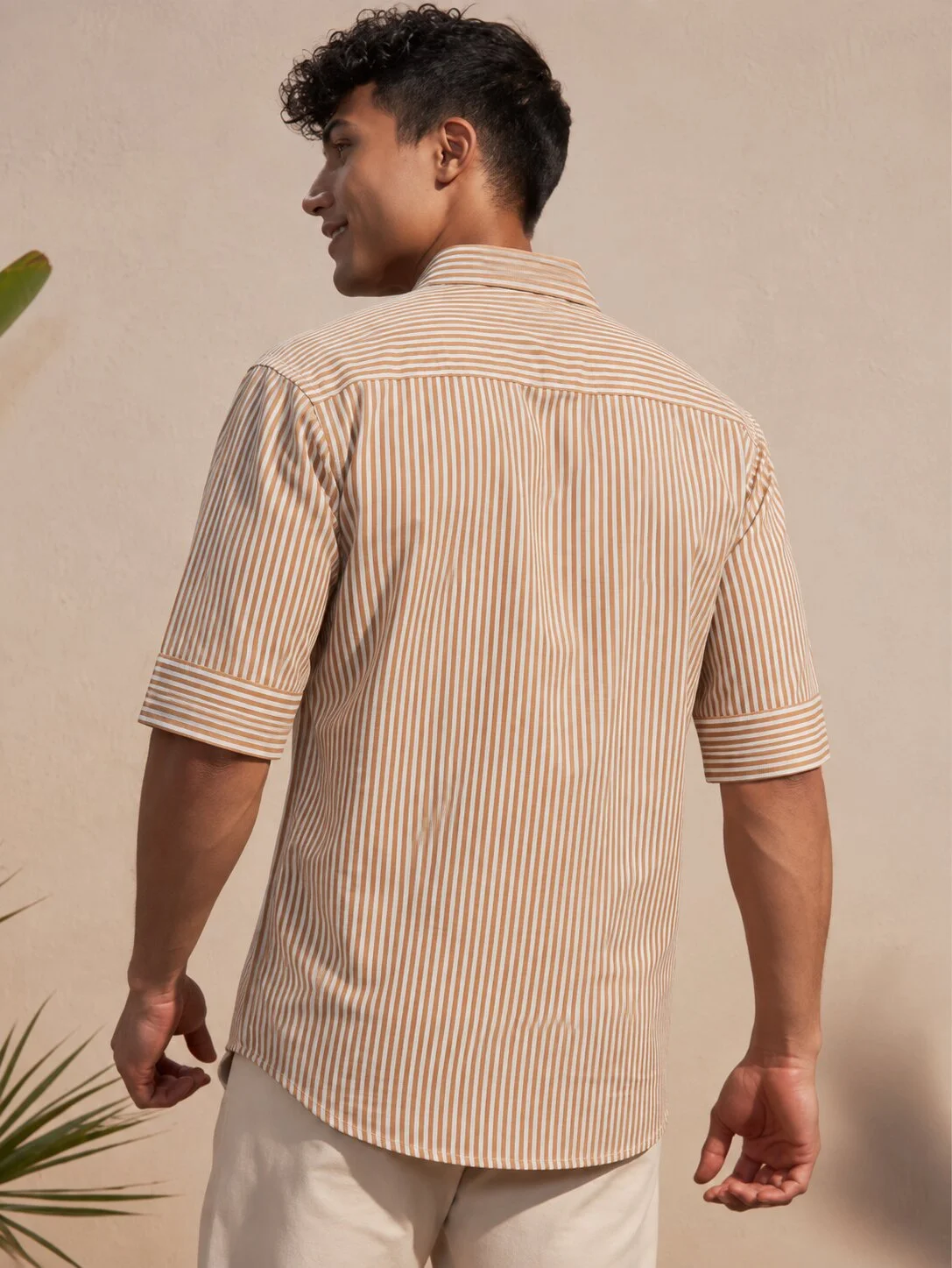 Back view of a male model wearing an orange and white striped short-sleeve shirt with a collar