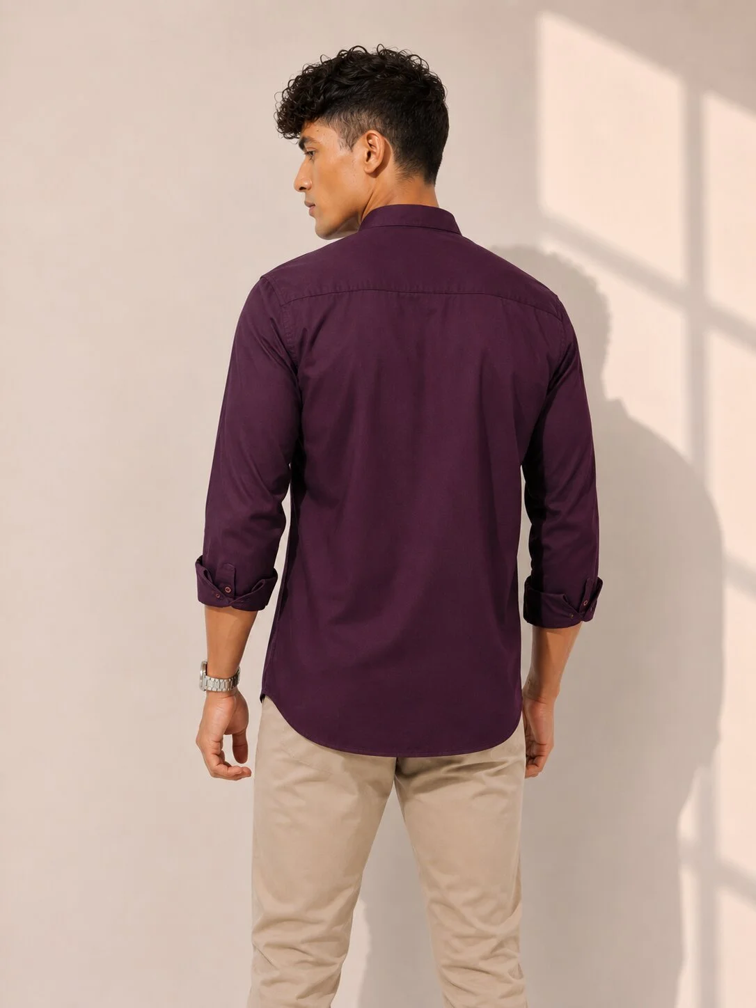 Back view of a male model wearing a wine purple solid shirt with rolled-up sleeves and beige trousers