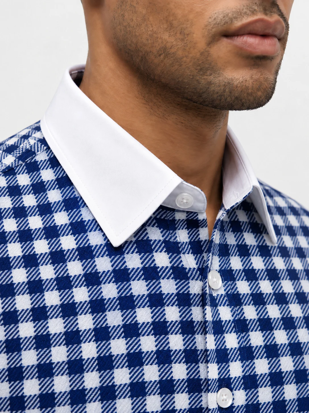 Close-up of a blue and grey checkered shirt on a model, featuring a plain collar and visible buttons