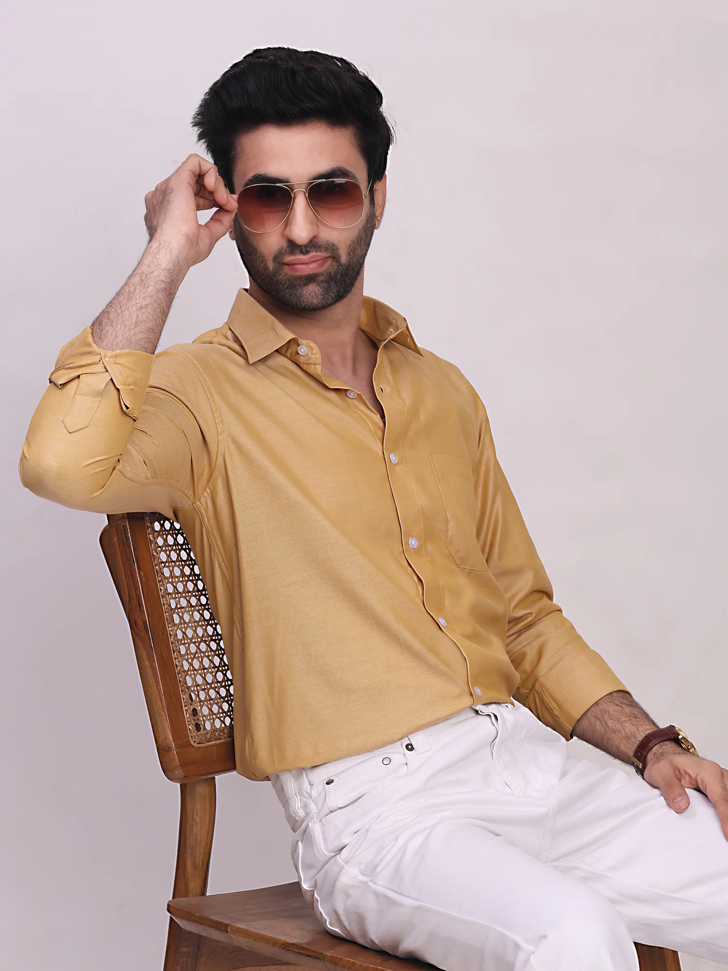 Golden yellow long-sleeve shirt with collar and front buttons, worn by a model sitting on a chair