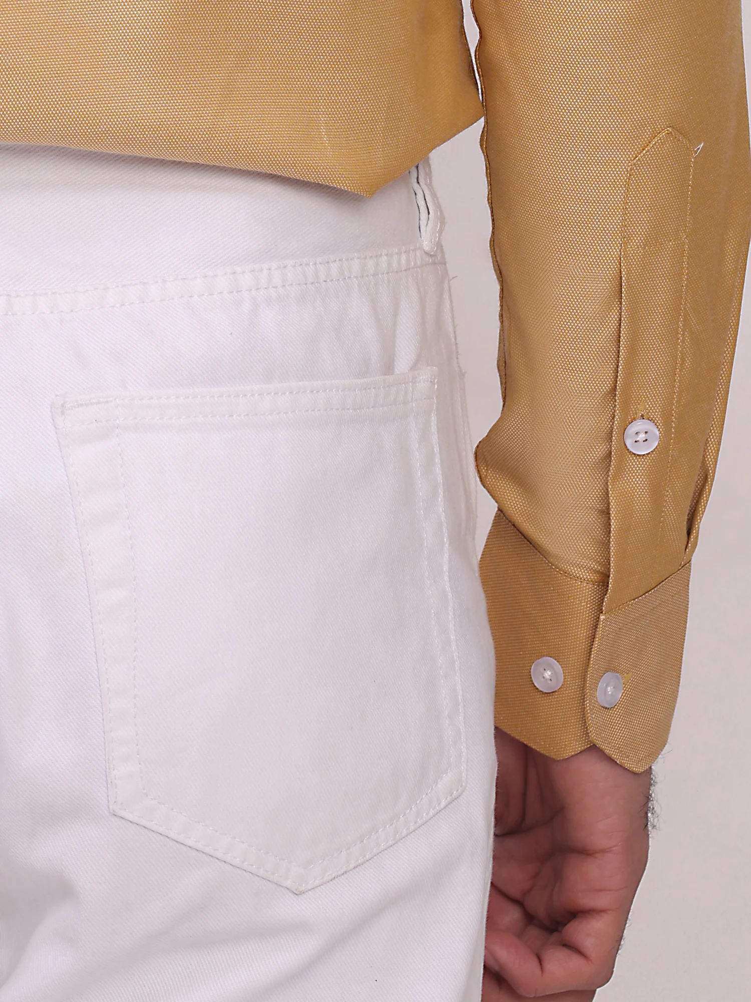 Close-up of golden yellow shirt sleeve with buttons paired with white trousers