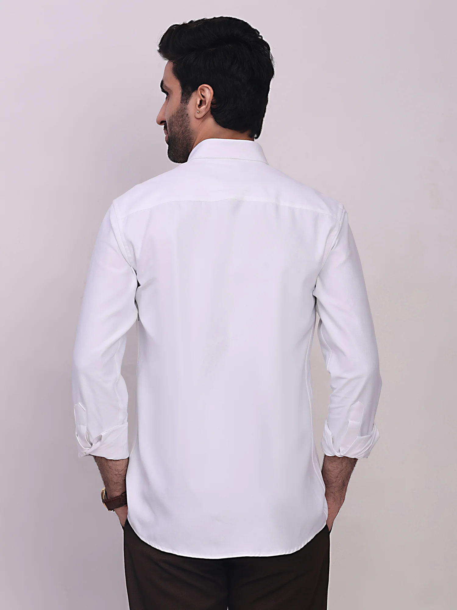 Back view of a male model wearing a solid white long-sleeve shirt with cuffs rolled up