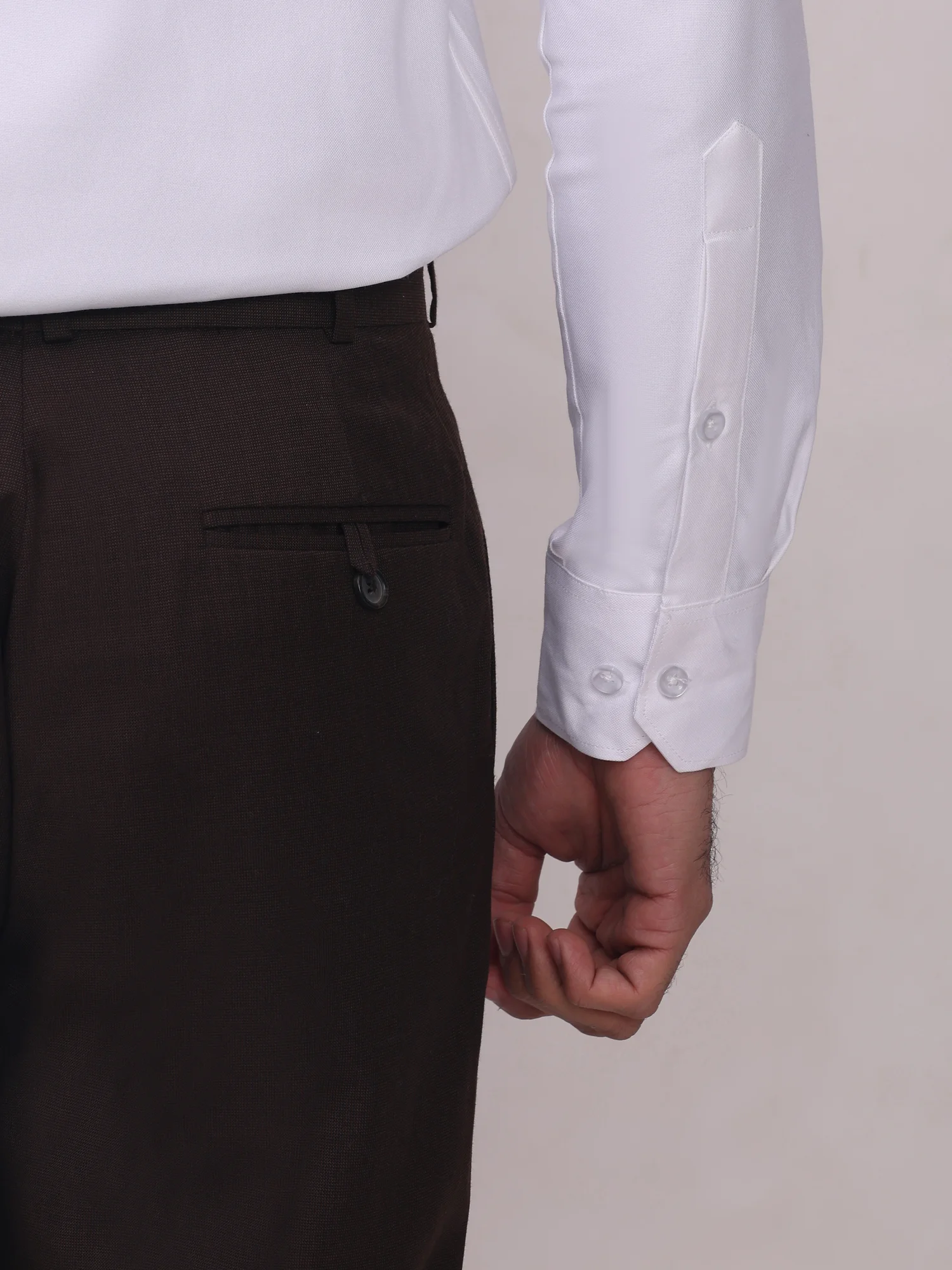 Close-up of a model wearing a white long-sleeve shirt with buttoned cuffs paired with dark brown trousers