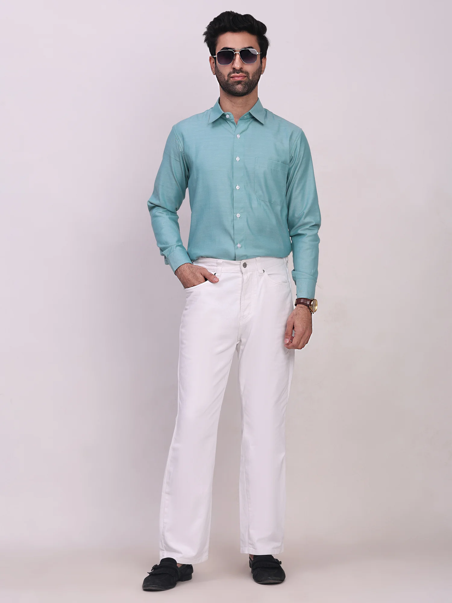Front view of a model wearing a sea green long-sleeve shirt with a collar, button placket, chest pocket, and white trousers