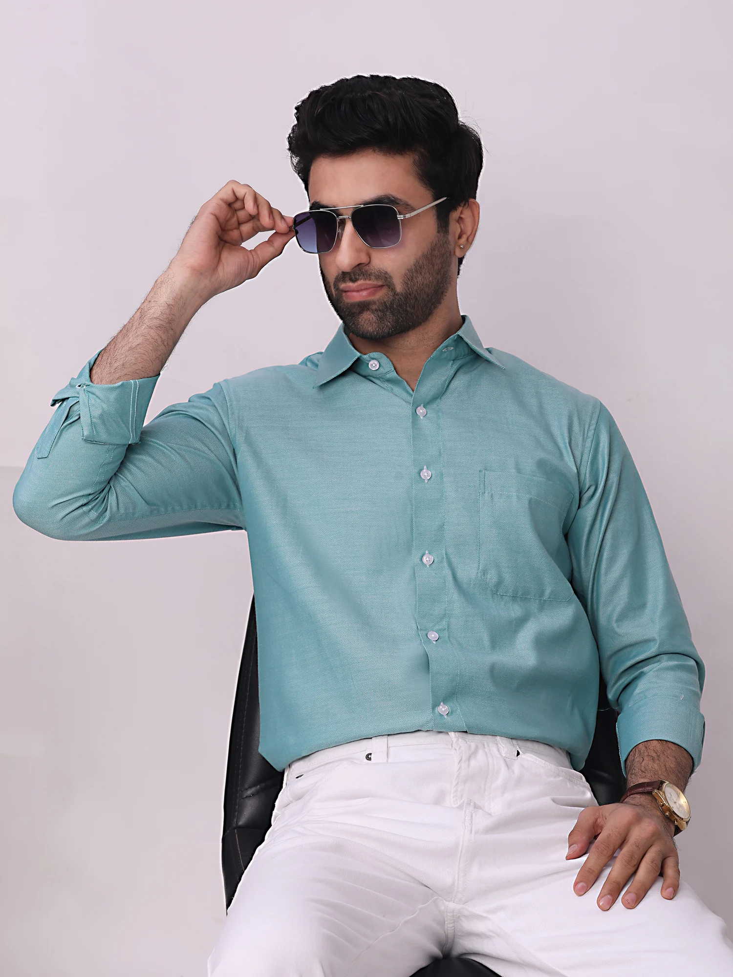 Model wearing a sea green long-sleeve shirt with collar, front buttons, and chest pocket, paired with white trousers