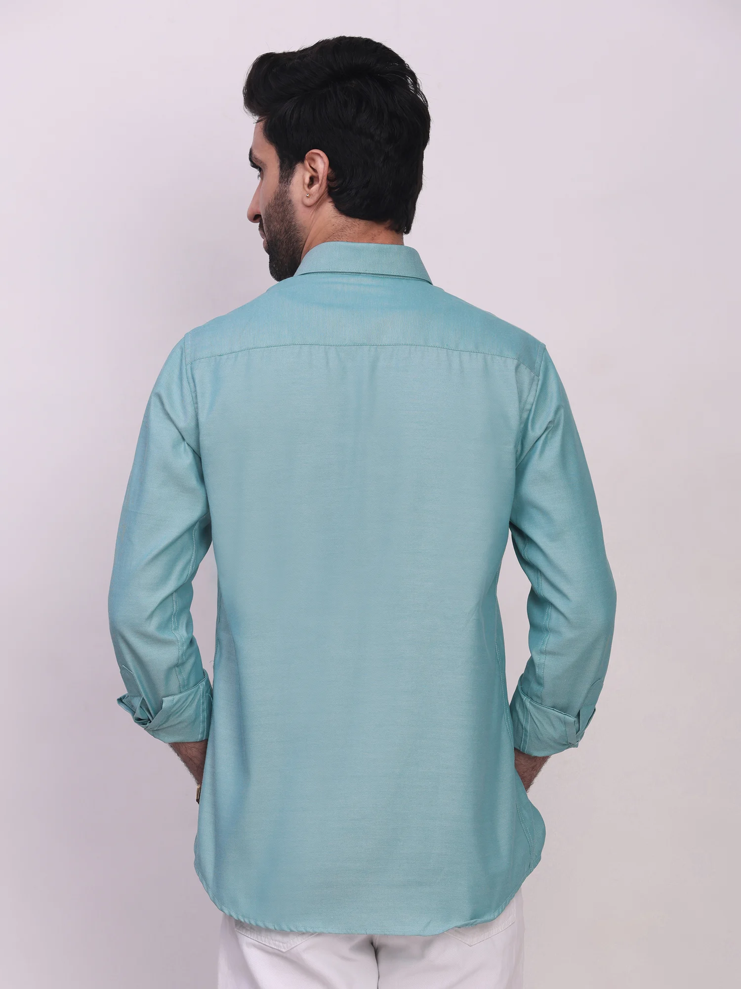 Back view of a model wearing a sea green long-sleeve shirt with rolled-up cuffs