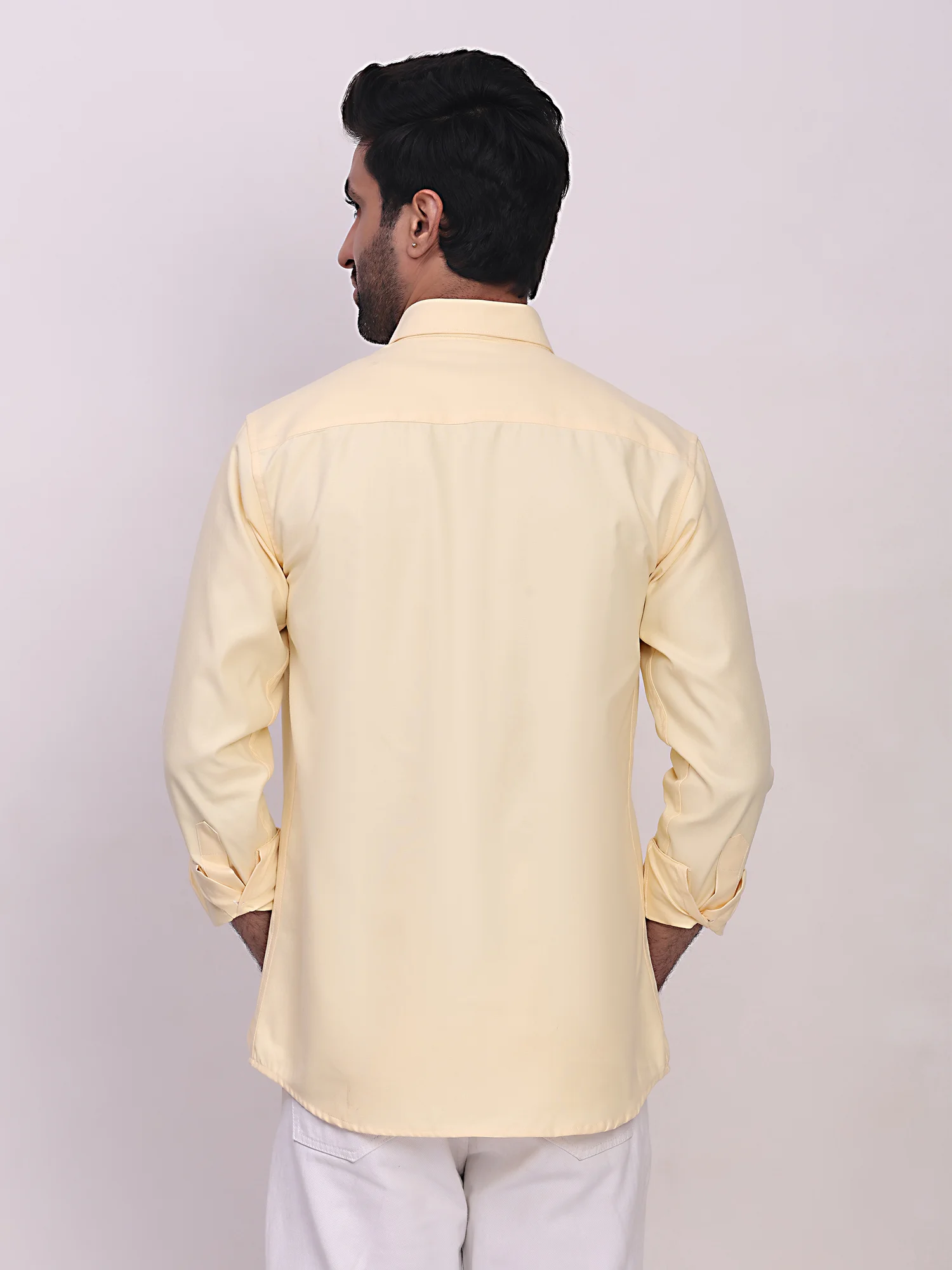 Back view of a male model wearing a light yellow long-sleeve shirt and white trousers