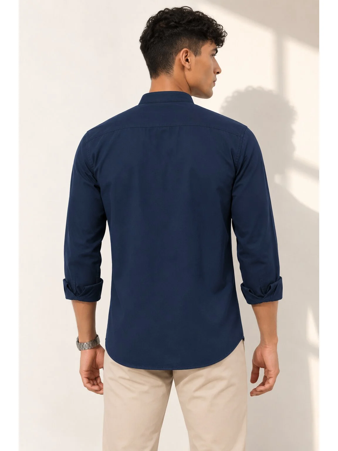 Back view of a male model wearing a solid navy blue long-sleeve shirt kurta and beige trousers