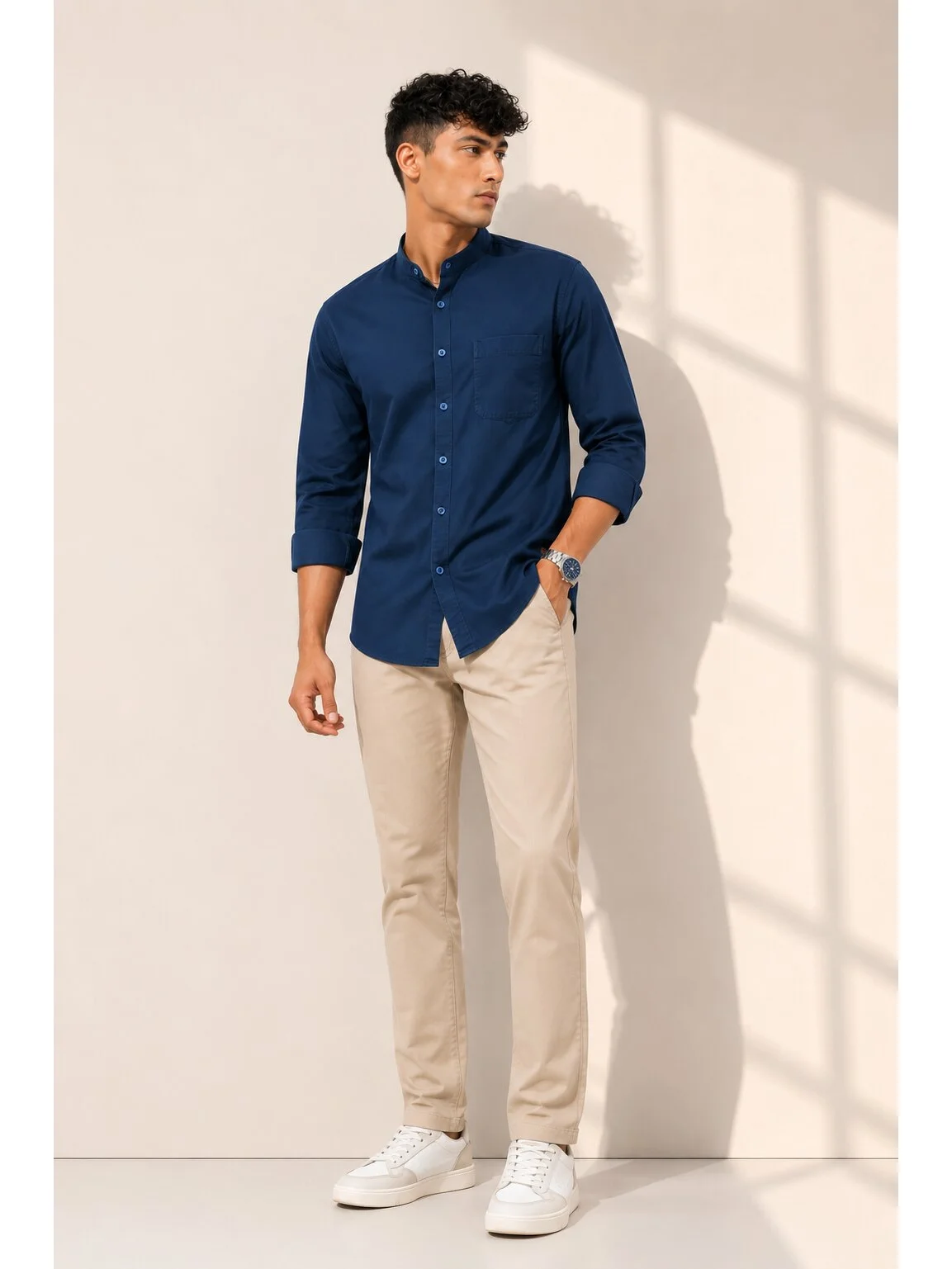 Model wearing a navy blue shirt with mandarin collar, chest pocket, and rolled-up sleeves, paired with beige trousers