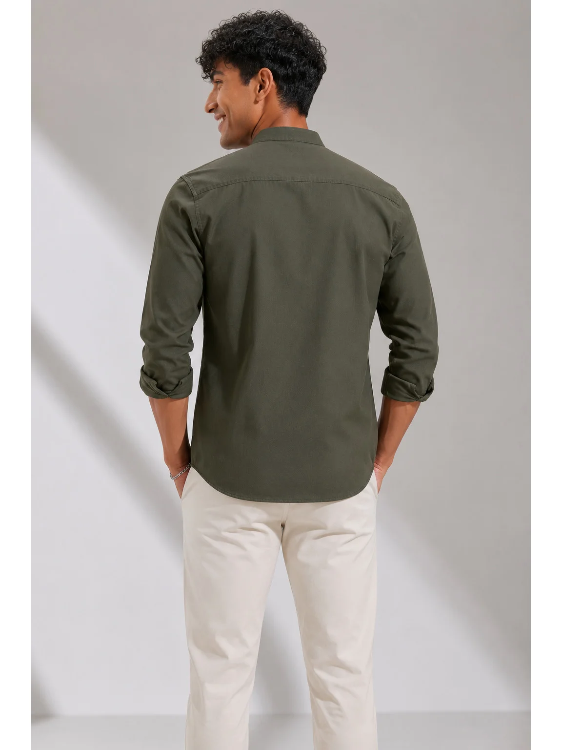 Back view of a male model wearing a dark olive green shirt and white trousers