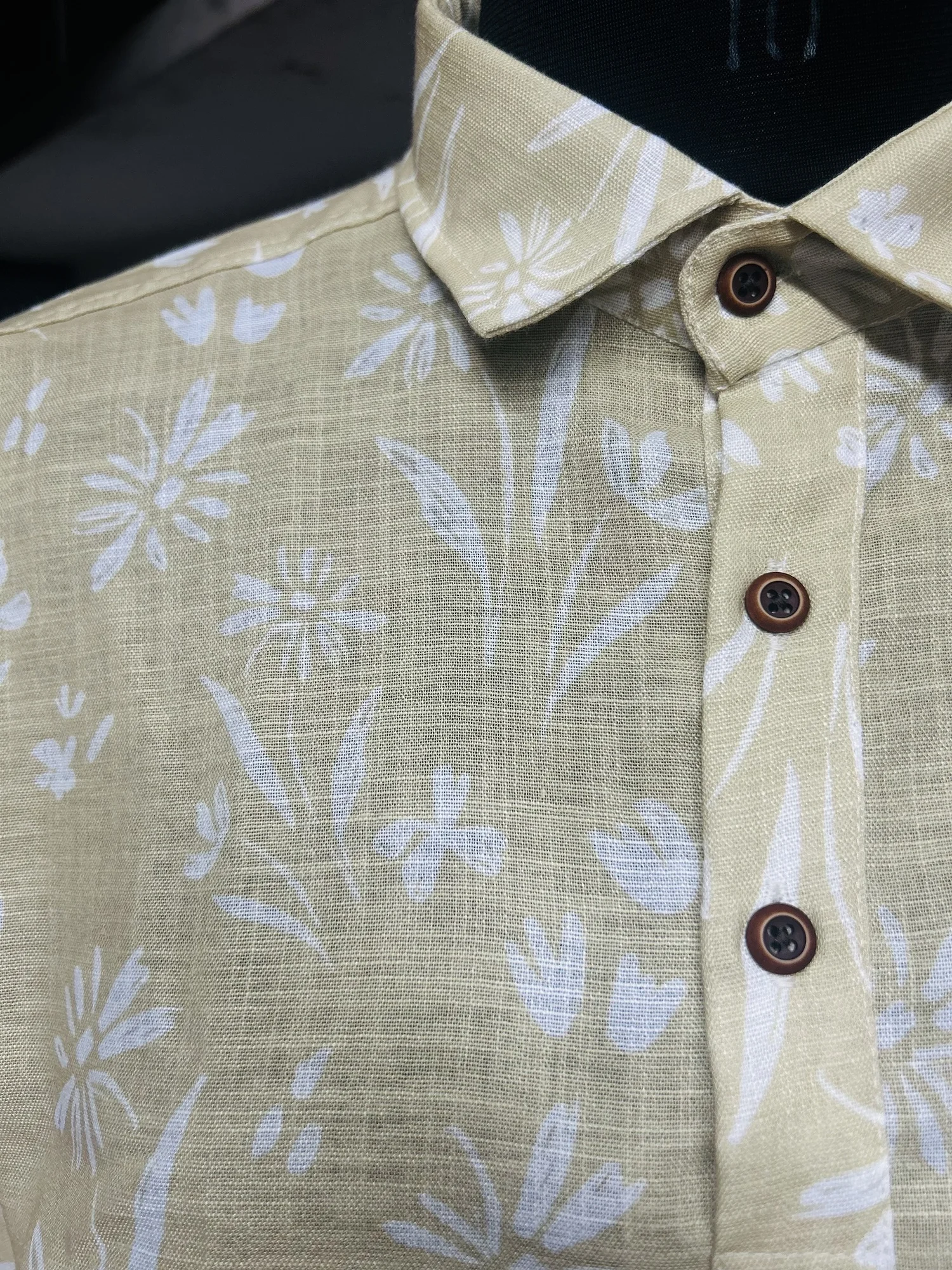 Close-up of pastel yellow shirt with white floral print, shirt collar, and dark brown buttons