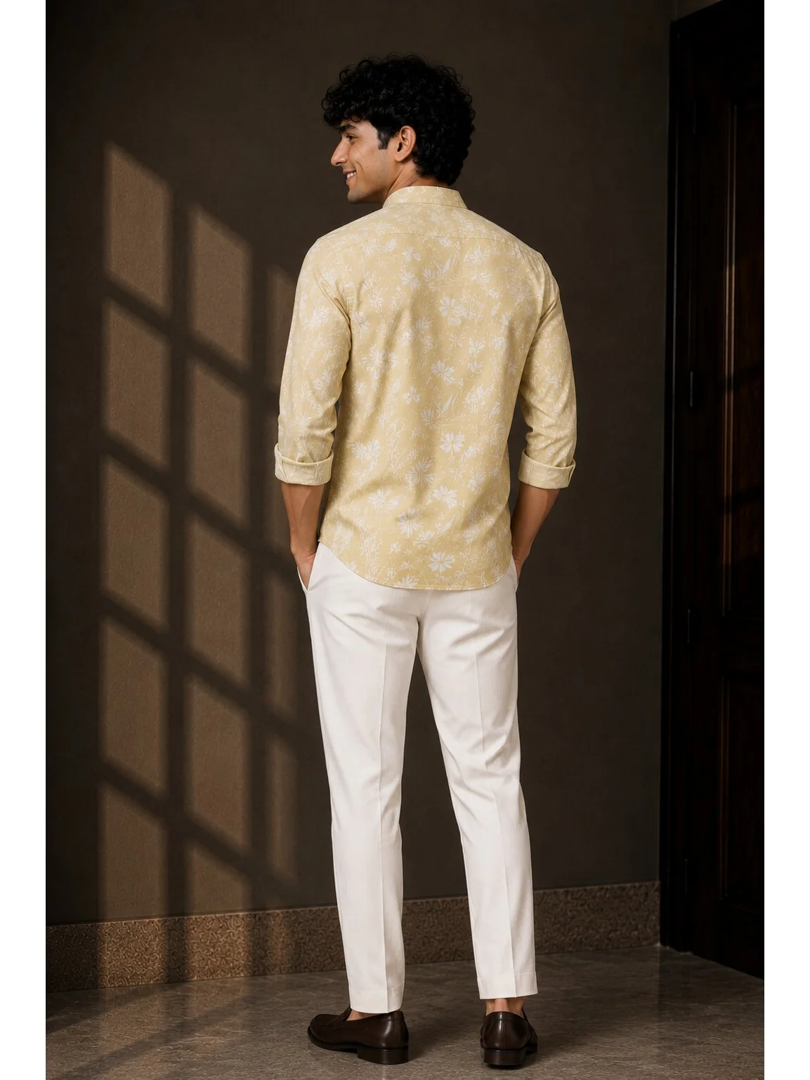 Model wearing a pale yellow short kurta with white floral print, full sleeves rolled up, and white trousers, back view