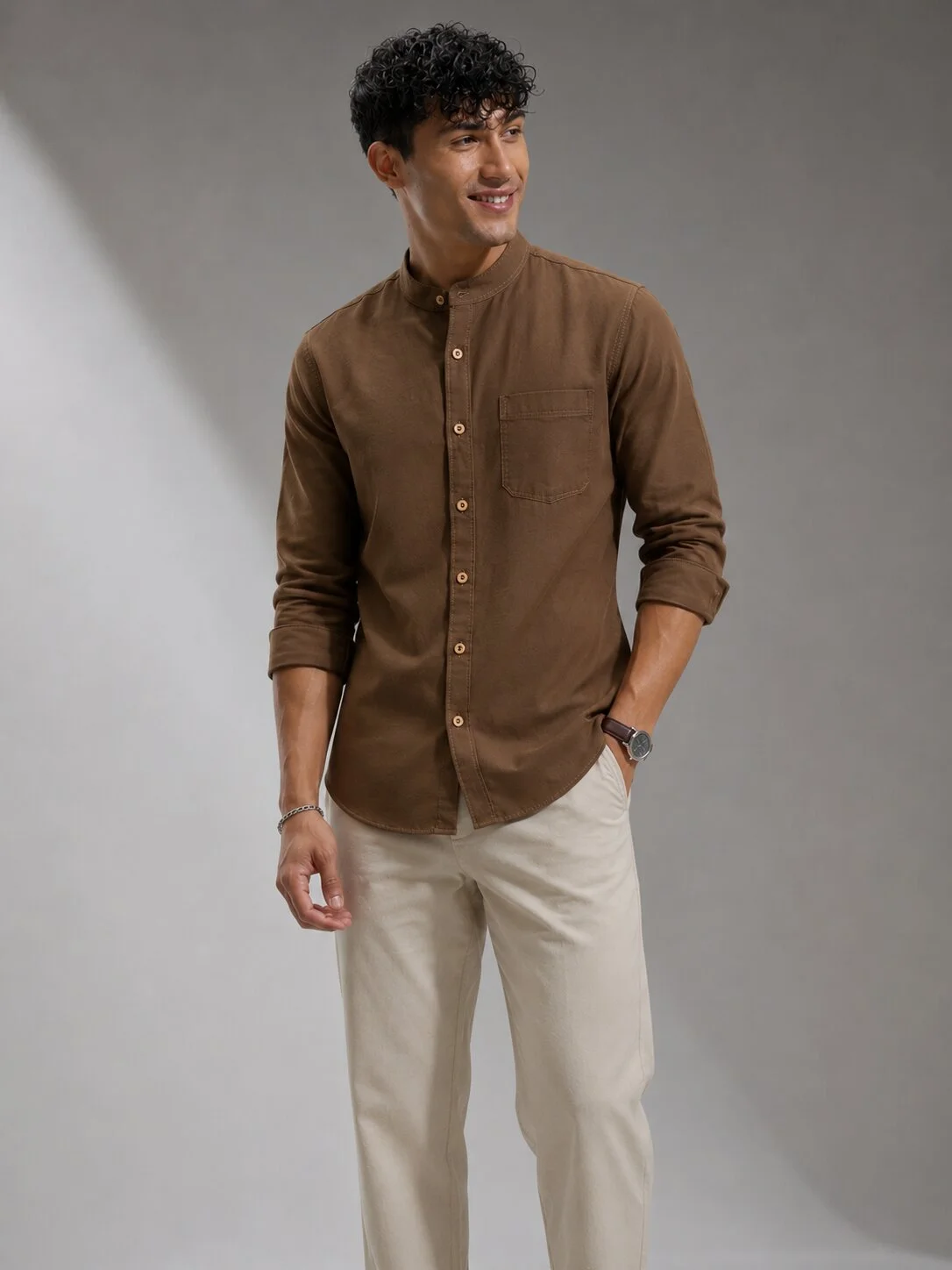 Brown kurta with mandarin collar, long sleeves, chest pocket, and buttons. Worn by a model