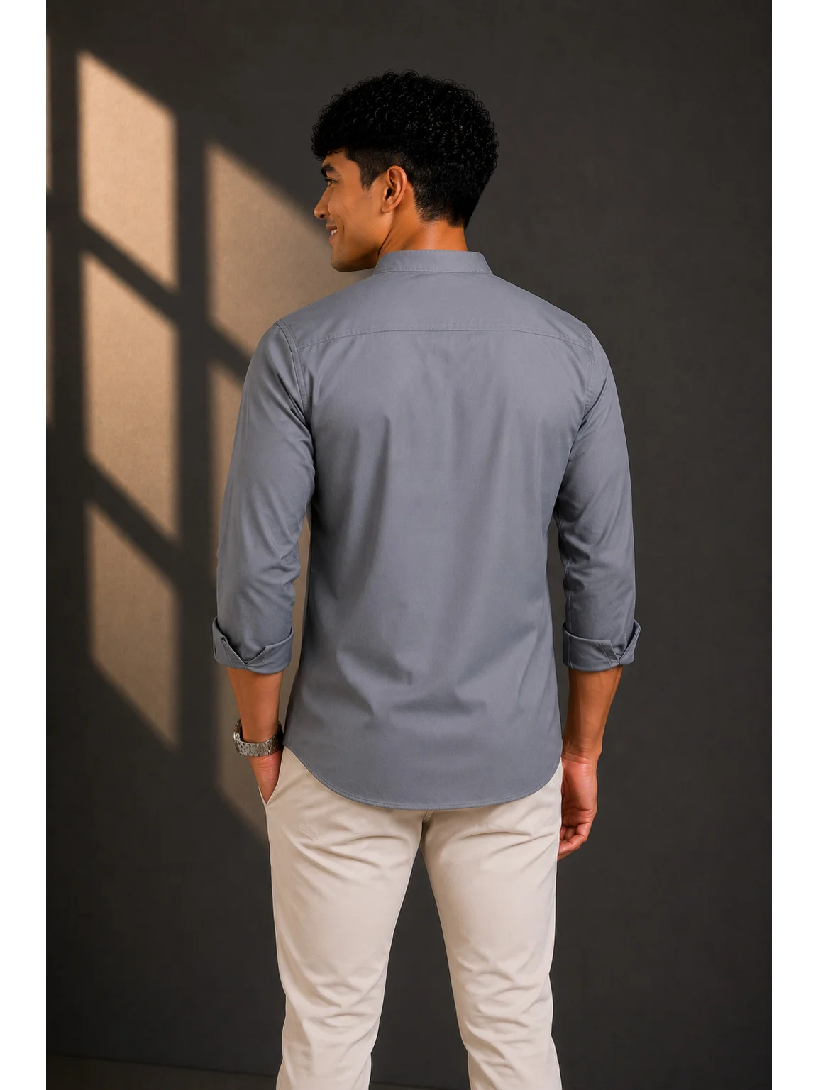 Back view of a male model wearing a charcoal grey short kurta with long sleeves and light trousers